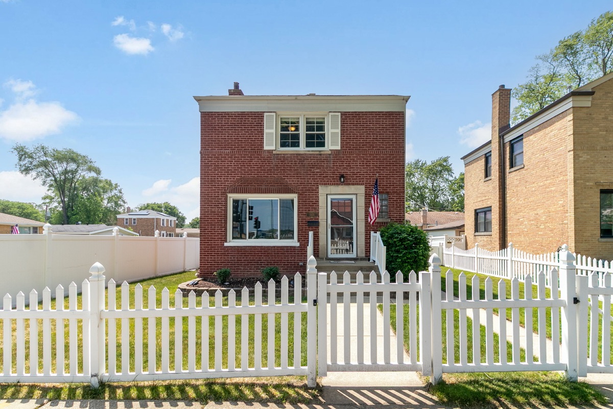 Red brick home with a white picket fence photographed in bright daylight