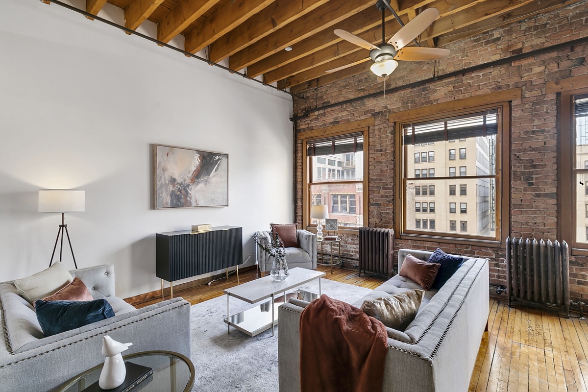 Sunlit loft living room with exposed brick, wood beams, and large windows